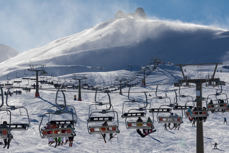 Verschillende skiliften met skiërs in, met uitzicht op een besneeuwde berg